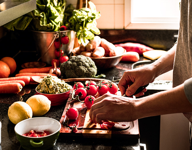 Image of a person prepping a meal in a kitchen filled with fresh vegetables.