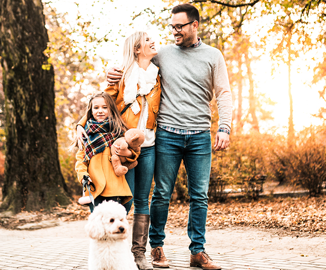 A smiling family and their dog standing outside in autumn