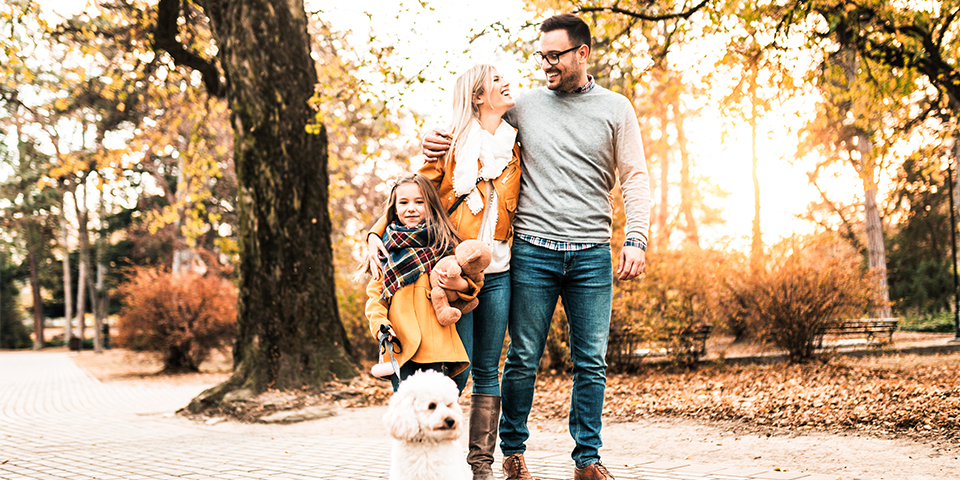 A smiling family and their dog standing outside in autumn