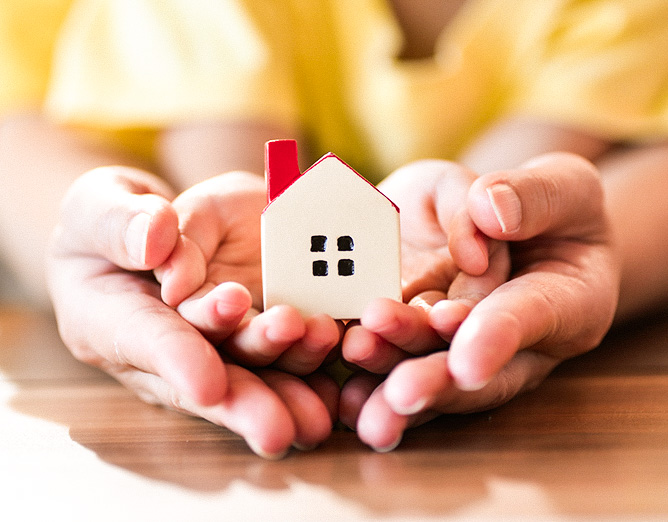 Image of two sets of hands holding a small ceramic house figurine.