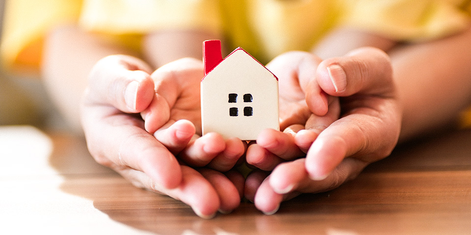 Image of two sets of hands holding a small ceramic house figurine.