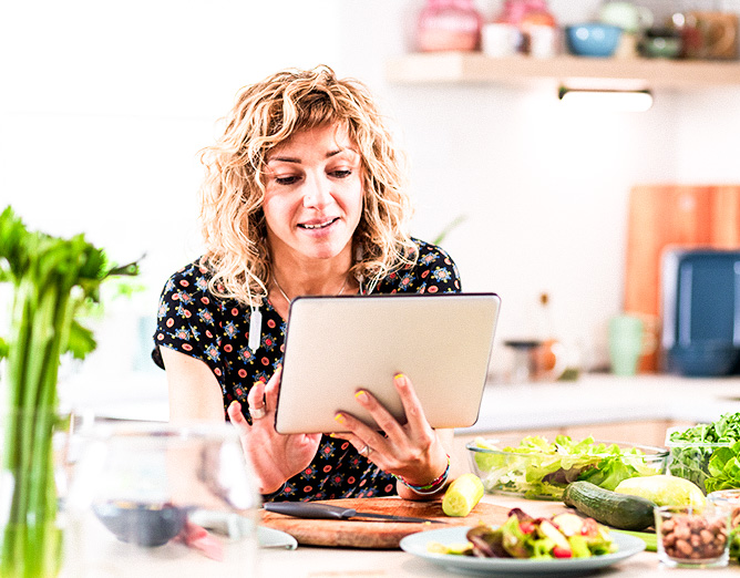 Image of a woman in a bright kitchen looking at a tablet and smiling.