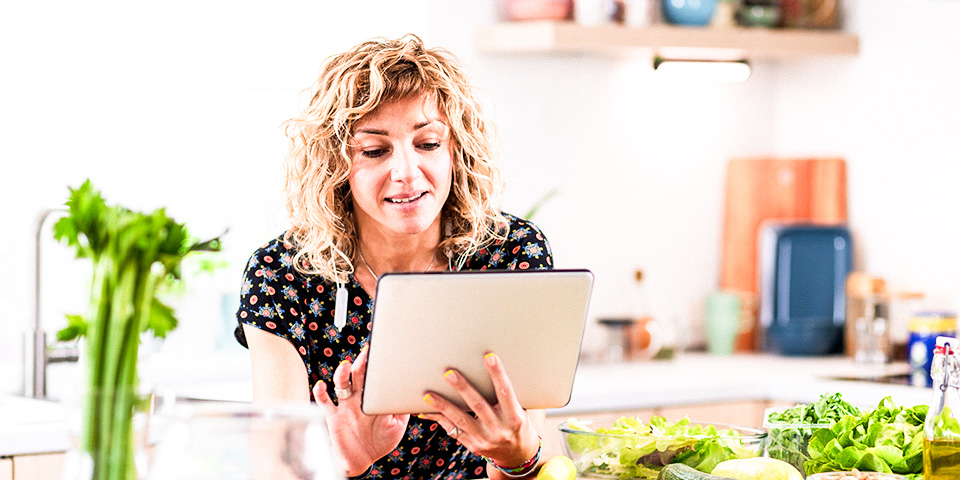 Image of a woman in a bright kitchen looking at a tablet and smiling.