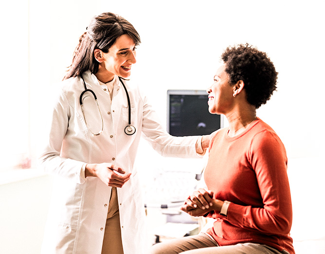 Image of a smiling female doctor touching the shoulder of a smiling female patient during a preventive care visit.