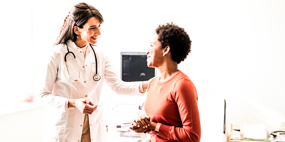 Image of a smiling female doctor touching the shoulder of a smiling female patient during a preventive care visit.