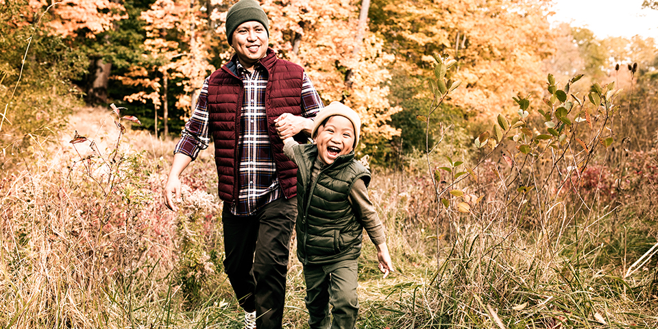 Father and kid on a forest walk, holding hands and laughing.