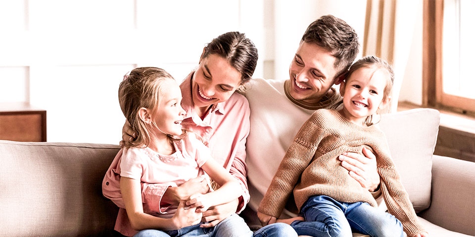 male and female adults sitting on couch with two young children sitting on laps