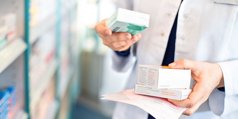 person in a white lab coat holding pharmacy merchandise