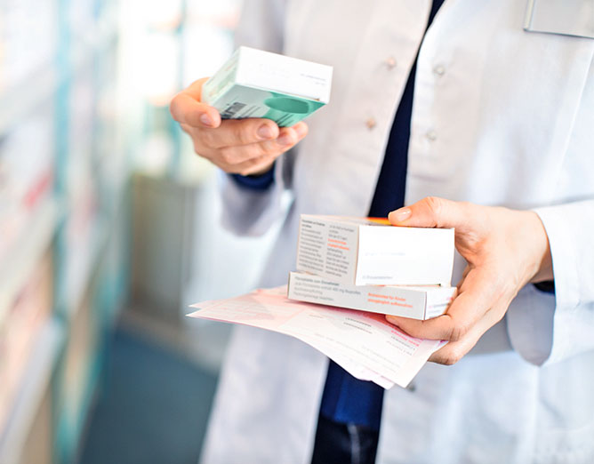 person in a white lab coat holding pharmacy merchandise